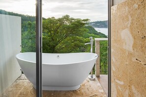 Uma banheira de imersão em uma varanda com vista panorâmica para uma floresta e um corpo d'água.