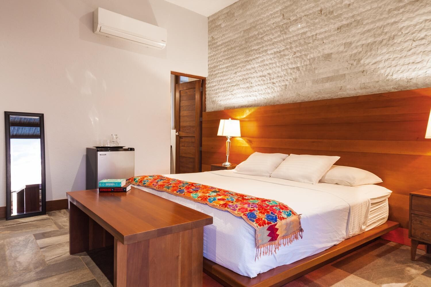 A hotel room with a bed, bedside table, lamp, and a small desk with a chair.