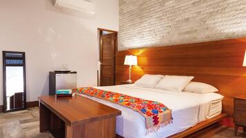A hotel room with a bed, bedside table, lamp, and a small desk with a chair.
