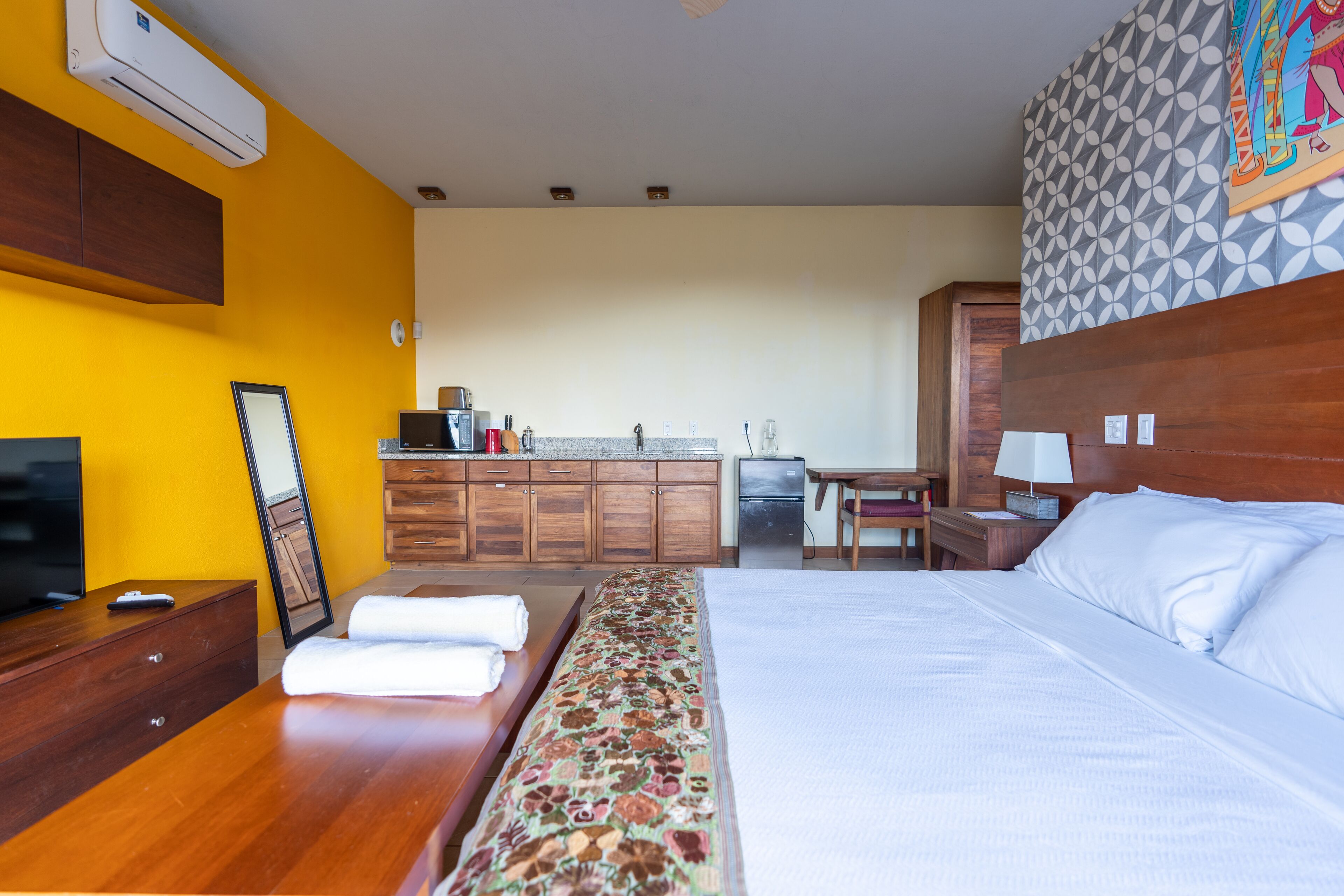 Una habitación de hotel con cama, televisión, escritorio y kitchenette.