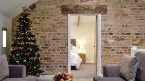 Une pièce chaleureuse avec un mur en briques, un sapin de Noël, un lit et une table basse sur laquelle sont posés des magazines.