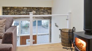 Une pièce chaleureuse avec un mur en pierre, un canapé, une porte vitrée donnant sur l’extérieur et un poêle à bois.