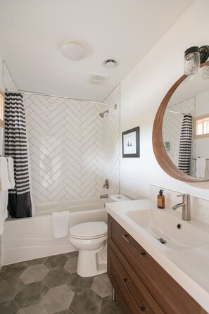 A modern bathroom with a white herringbone tile backsplash, a freestanding bathtub, a toilet, a vanity with a mirror, and a shower curtain. - LE CHALET WATERFRONT RETREAT - Great view & location! (Ucluelet)