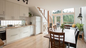 Une cuisine moderne avec des meubles blancs, une table à manger en bois et un escalier menant à un balcon.