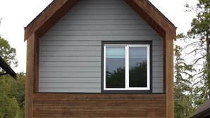 Une maison à deux étages, à l’extérieur gris et aux ornements en bois. On y voit une enseigne indiquant « Stationnement du studio » et une autre pour « Le Chalet, un havre de paix au bord de l’eau ».