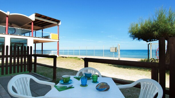 Una mesa frente a la playa, con vista al mar, una valla de madera y un edificio con balcón.