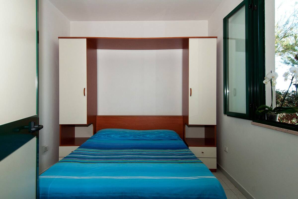 A bedroom with a bed, a wardrobe, and a window with a plant.
