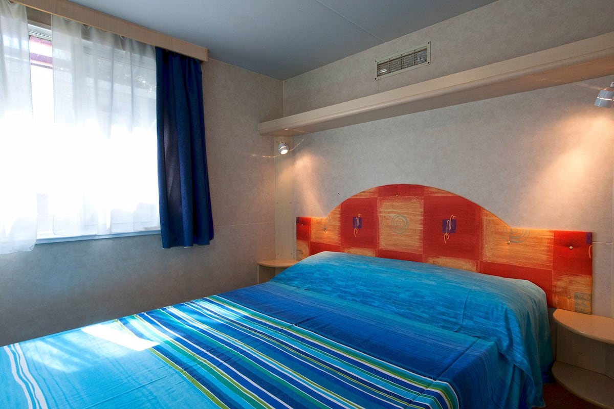 A hotel room with a bed, a window with curtains, and a headboard with built-in lighting.