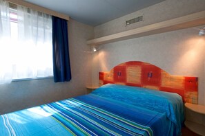 Una habitación de hotel con cama, ventana con cortinas y cabecera con iluminación integrada.