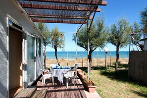Un porche cubierto con una mesa y sillas, con vista a la playa.