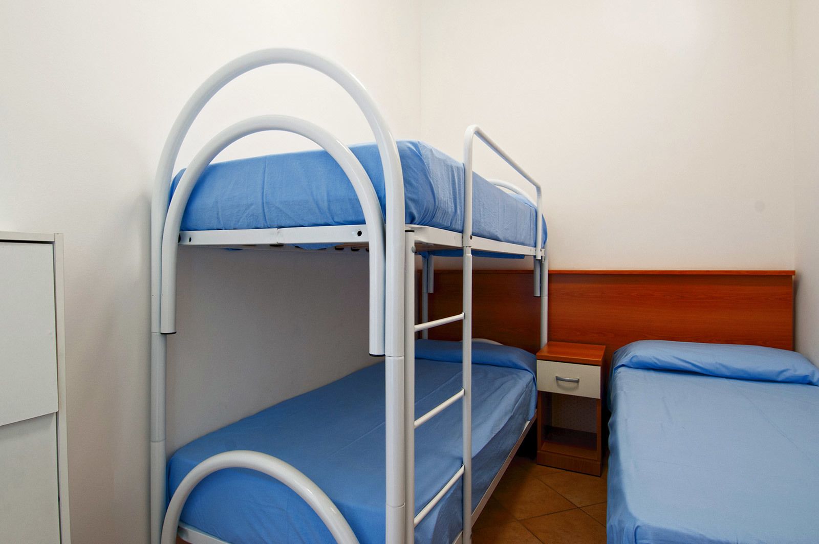 Camera con letto a castello, una branda in legno, un letto singolo e un piccolo comodino.