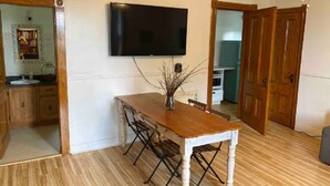 A dining area with a wooden table and chairs, a flat-screen TV mounted on the wall, and a wooden door. - Family Wellness Space on 4 acres (Kensington)
