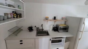 A compact kitchen with a sink, toaster, and microwave. There are white cabinets and a shelf with various items. - Family Wellness Space on 4 acres (Kensington)