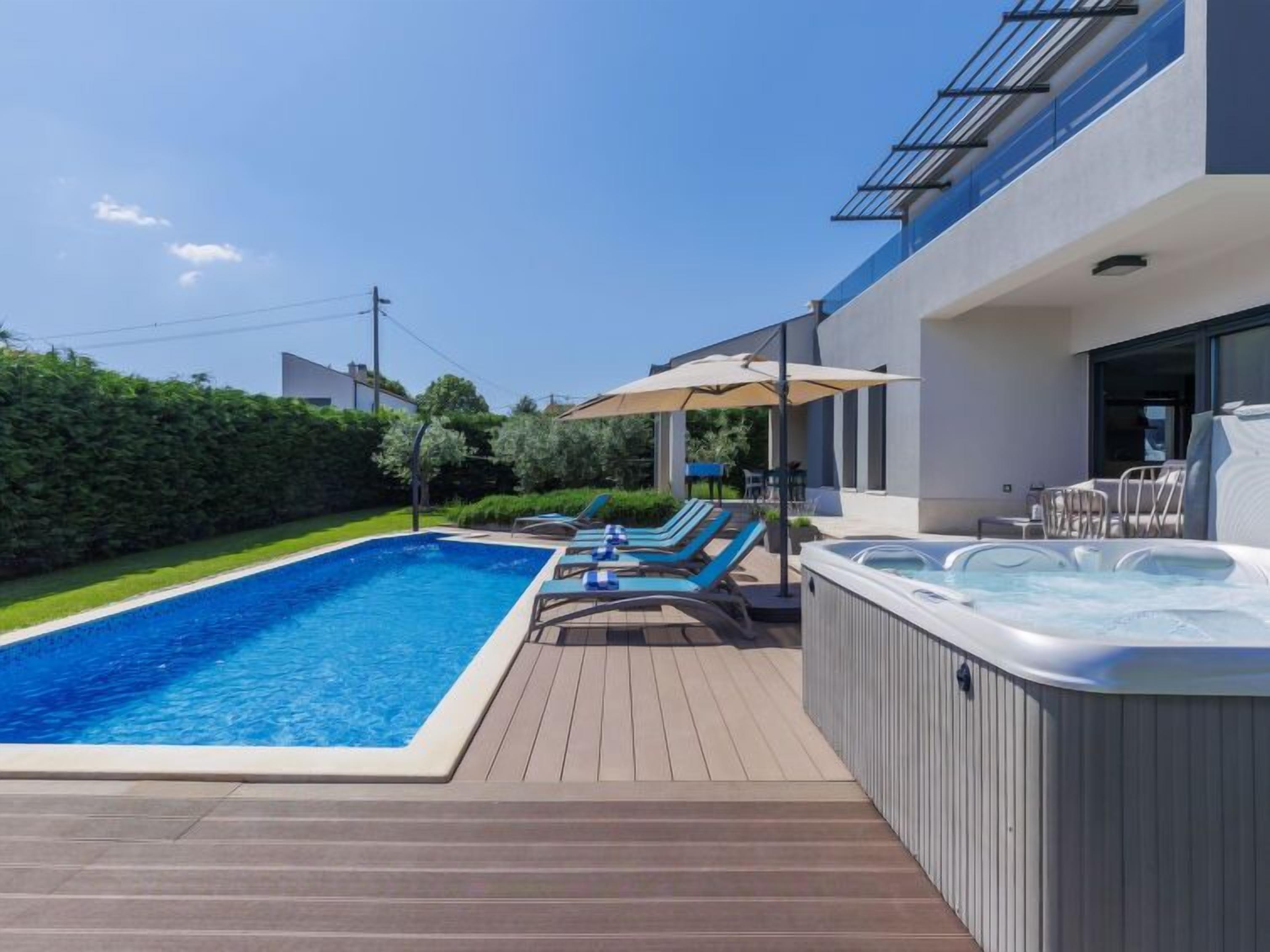 Un espace piscine extérieur moderne, doté d’un jacuzzi, de chaises longues et d’une terrasse en bois.