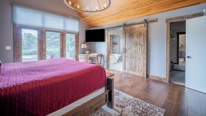 Une chambre avec un grand lit, un plafond en bois et un téléviseur fixé au mur.