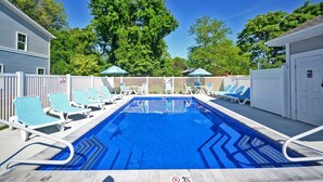 Una piscina rectangular con agua azul, rodeada de sillones de descanso blancos y sombrillas.