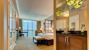 Camera d'albergo con un letto grande, una scrivania, una sedia, una panca, un minibar e vista sulla città attraverso ampie finestre.
