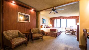 A hotel room with a bed, two armchairs, a desk, and a ceiling fan.