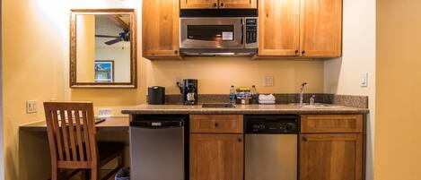 A compact kitchen with wooden cabinets, a stainless steel microwave, a dishwasher, and a coffee maker.