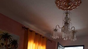 A room with a bed, a chair, a painting of palm trees, a chandelier, and a door leading outside. - Hotel Hamilton - Kaly Center (Hammamet)