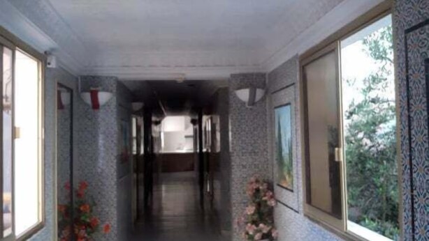 A corridor with patterned walls and tiled flooring, leading to a room with a window and a door. - Hotel Hamilton - Kaly Center (Hammamet)