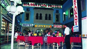 A bustling indoor dining area with tables covered in red tablecloths, a visible snack bar, and a pizza restaurant. - Hotel Hamilton - Kaly Center (Hammamet)