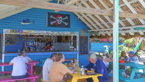 A beachside bar with outdoor seating and a thatched roof. - Reef House (Roatan)