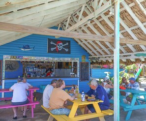 Un bar en la playa con terraza y techo de paja.
