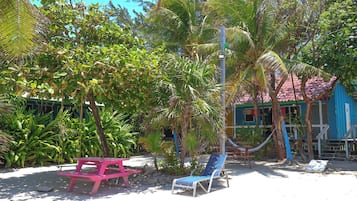 Una zona de playa con una hamaca, una silla de descanso azul y una mesa de picnic rosa.