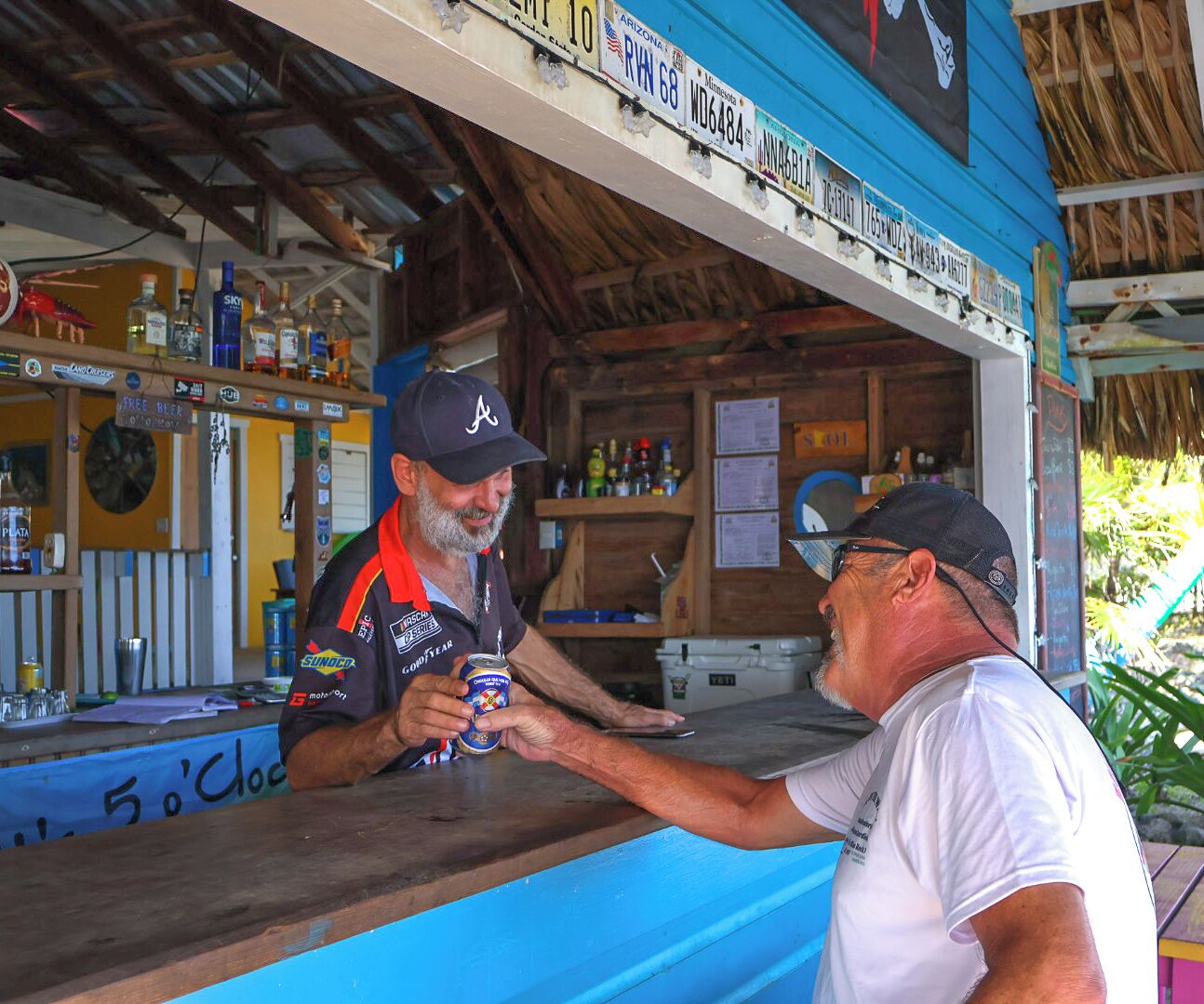 Un bar con mostrador azul, estanterías de madera con diversas botellas y un letrero sobre el mostrador.