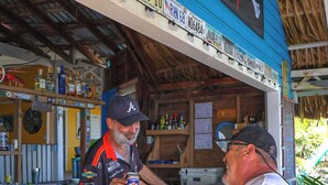 A bar with a blue counter, wooden shelves with various bottles, and a sign above the counter. - Reef House (Roatan)