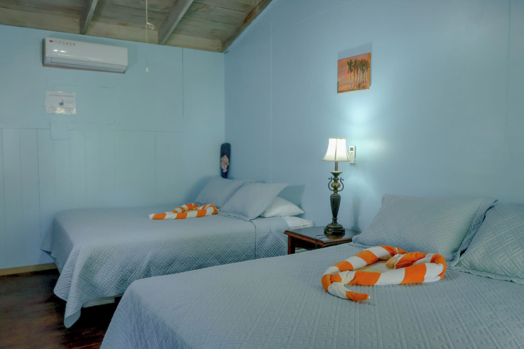 Una habitación con dos camas, una mesita de noche, una lámpara y un cuadro en la pared.