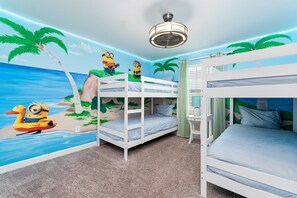 A room with bunk beds, a mural of a beach scene, and a ceiling fan.