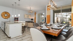 Una cocina moderna con una isla central, comedor con una mesa de madera preparada para seis personas y un amplio ventanal con vistas al exterior.