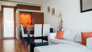 A modern living room with a white sofa, a dining table with chairs, and a kitchen area with a wooden cabinet.