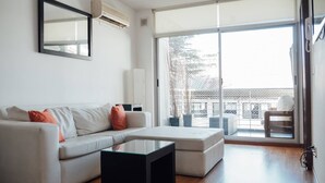 A modern living room with a sofa, a glass coffee table, and a large sliding glass door leading to a balcony.