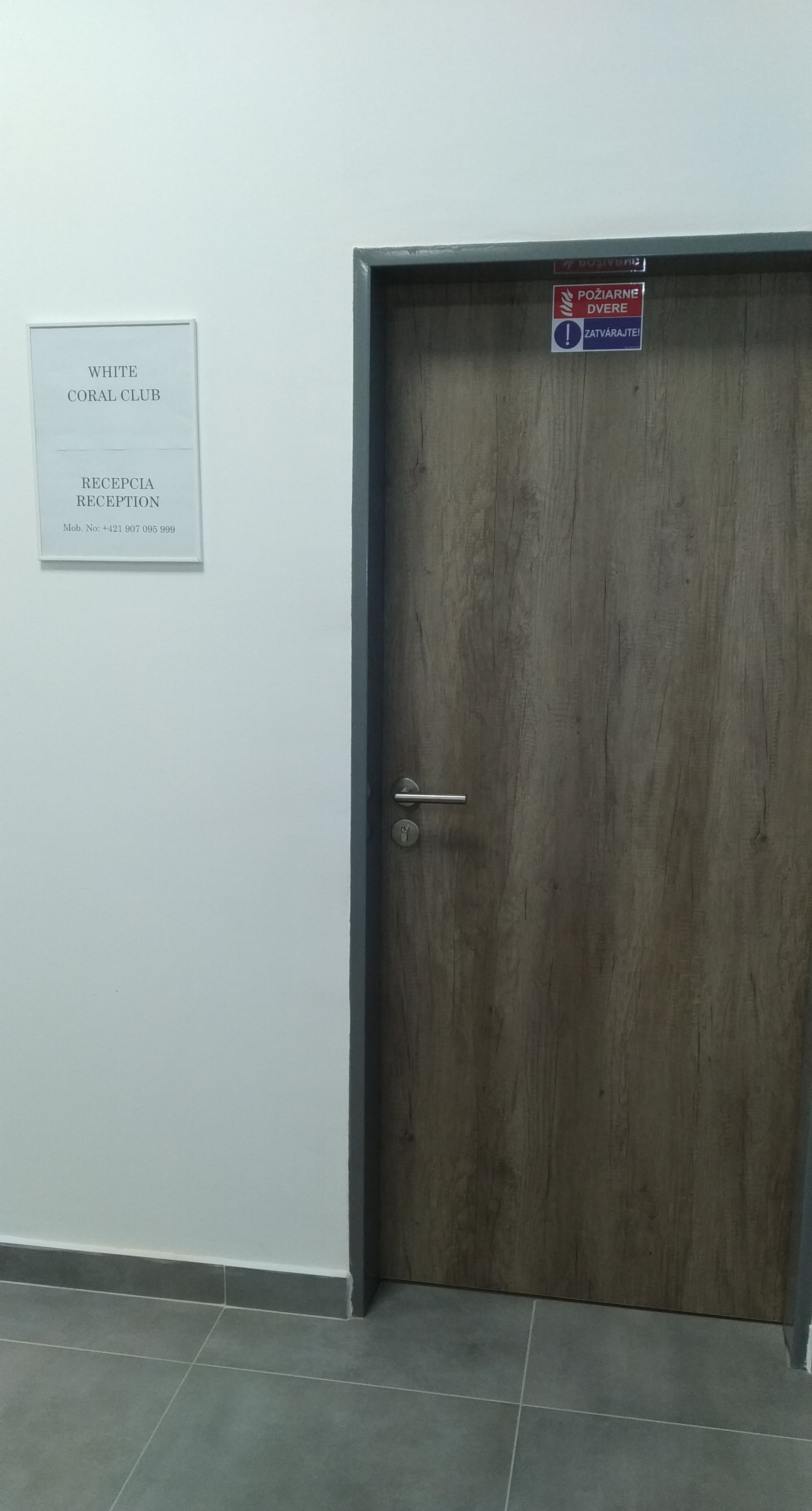 Zona de recepción con puerta de madera, cartel que indica White Coral Club y mostrador de recepción con un número de teléfono.