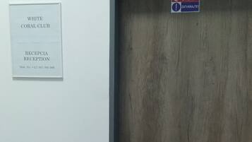 Zona de recepción con puerta de madera, cartel que indica White Coral Club y mostrador de recepción con un número de teléfono.