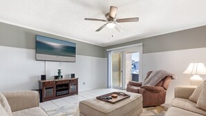 A living room with a ceiling fan, a flat-screen TV, a sofa, an ottoman, and a chair. - Allendale Docks * Pet Friendly! Boat Dock on Holiday Isle * Salt Water Vacations (Destin)