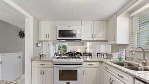 A kitchen with white cabinets, a microwave, a stove, and a sink. - Allendale Docks * Pet Friendly! Boat Dock on Holiday Isle * Salt Water Vacations (Destin)