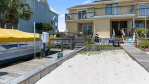 A beachfront property with a wooden dock, a covered boat, and a two-story building with balconies. - Allendale Docks * Pet Friendly! Boat Dock on Holiday Isle * Salt Water Vacations (Destin)