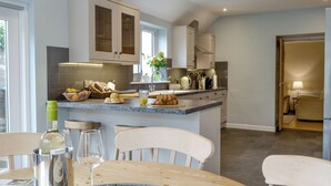 A modern kitchen with a dining area, featuring a central island, white cabinetry, and a view into the adjacent living space. - 3 bedroom accommodation in Gatehouse of Fleet, near Kirkcudbright (Gatehouse of Fleet, near Kirkcudbright)