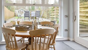 A dining area with a round table, wooden chairs, and a view of the garden through large windows. - 3 bedroom accommodation in Gatehouse of Fleet, near Kirkcudbright (Gatehouse of Fleet, near Kirkcudbright)