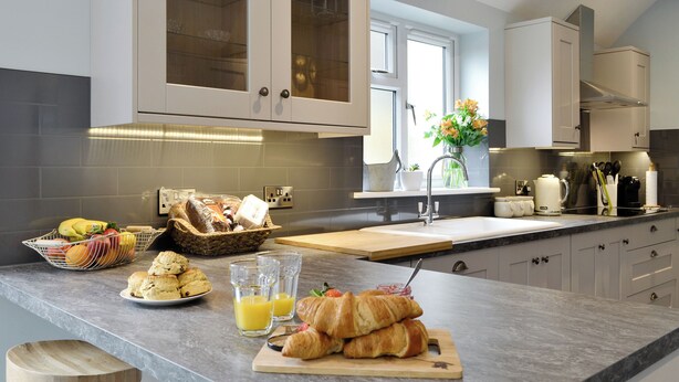 A modern kitchen with a marble countertop, wooden stools, and a breakfast spread including croissants, juice, and a fruit basket. - 3 bedroom accommodation in Gatehouse of Fleet, near Kirkcudbright (Gatehouse of Fleet, near Kirkcudbright)