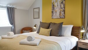 A neatly made bed with rolled towels, a bedside table with a lamp, and a painting of a street scene on the wall. - 3 bedroom accommodation in Gatehouse of Fleet, near Kirkcudbright (Gatehouse of Fleet, near Kirkcudbright)