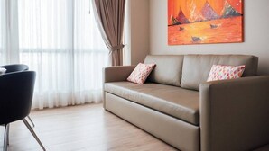 Un salon moderne avec un canapé beige, deux coussins à motifs, un fauteuil noir et un tableau représentant un coucher de soleil sur des montagnes, accroché au mur.