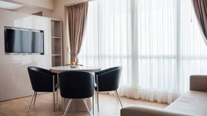 Un salon moderne avec un téléviseur à écran plat fixé au mur, une table de salle à manger ronde avec deux chaises et un canapé.