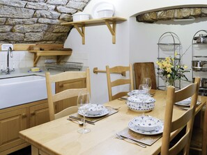 Un coin repas avec un mur en pierre, des chaises en bois et une table en bois dressée avec des assiettes, des verres et des couverts.