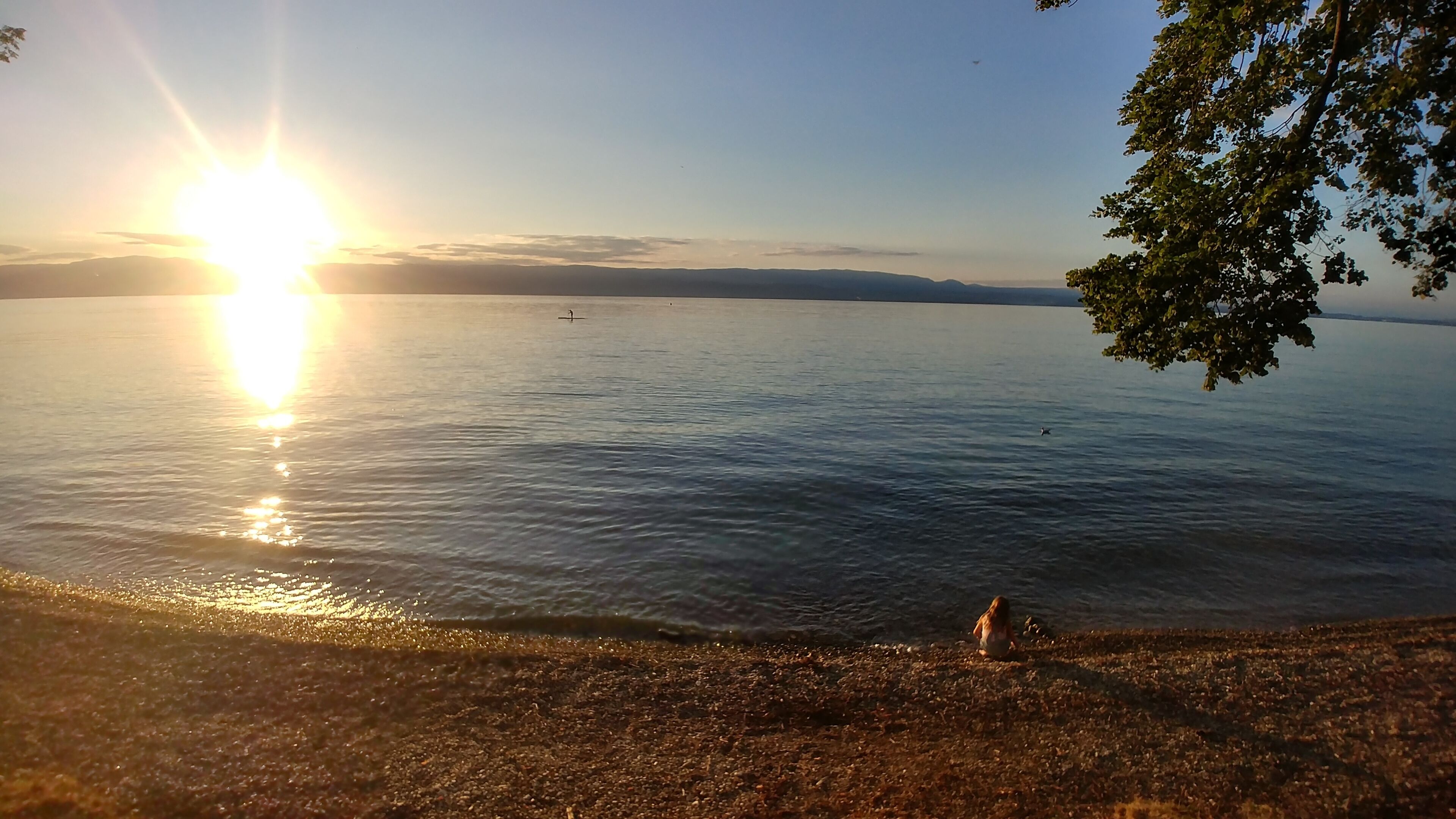 A calm lake with a clear sky and a sun reflecting on the water.