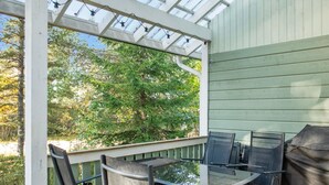 A covered outdoor seating area with a glass table and metal chairs, overlooking a wooded area.